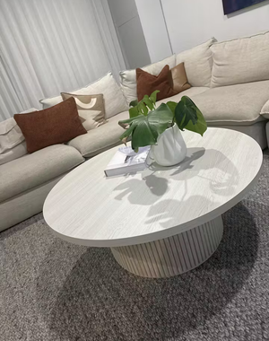 White round coffee table with vase and books in front of beige sofa.”