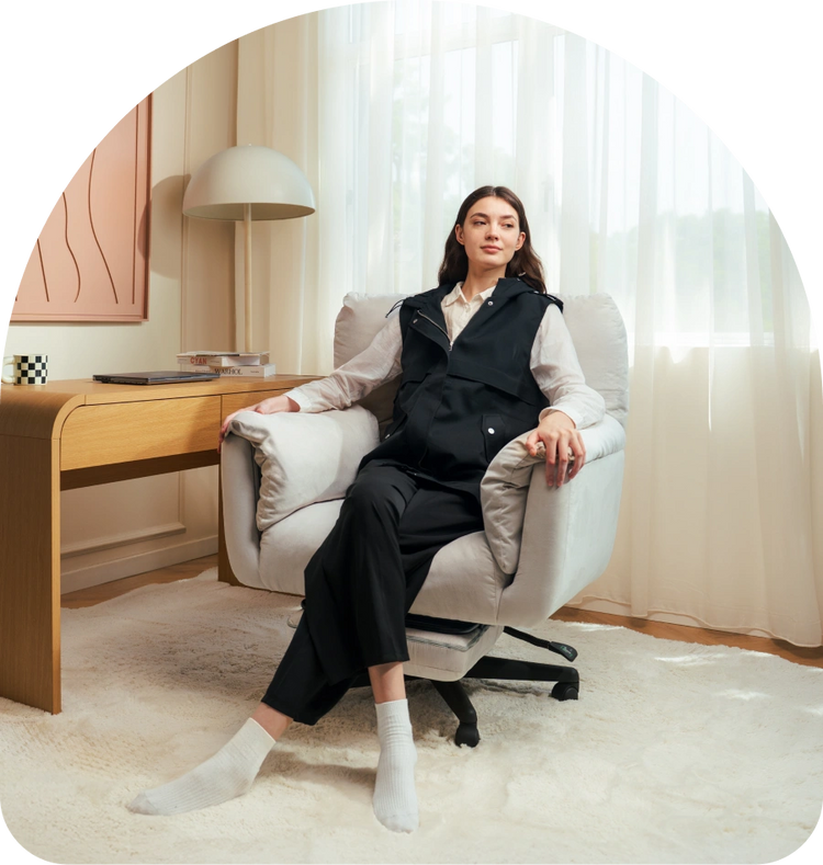 Woman sitting in a modern office chair in a well-lit room with a desk and lamp.